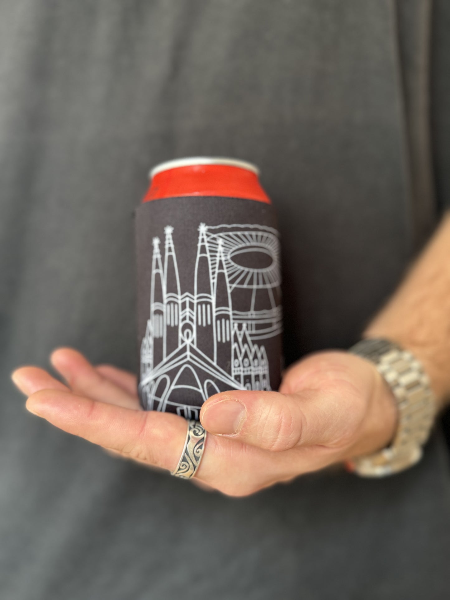 Man holding Sagrada Familia and Camp Nou line art souvenir on black neoprene koozie / killer koozys / stubby holder