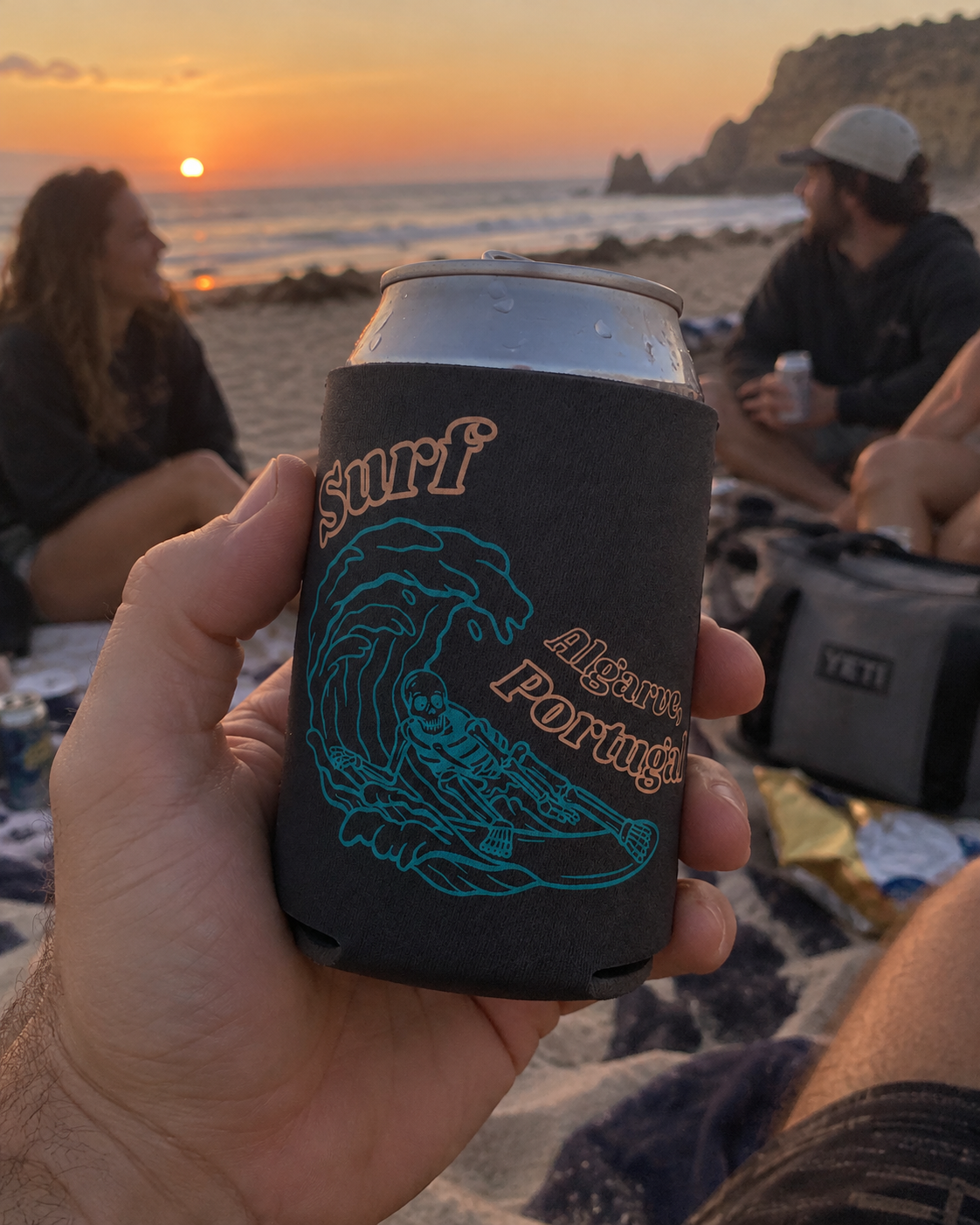 Surf Algarve Black koozy held up at a sunset beach hangout